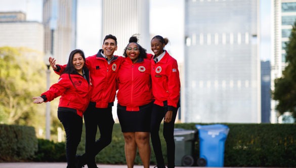 A group of AmeriCorps members pose together in the park with the skyline in the background.