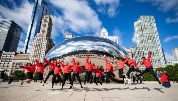 A group of AmeriCorps members jump and cheer in front of the city skyline.