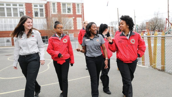 A group of AmeriCorps members chat as they walk across the school playground.