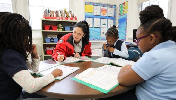 Three students listening at a table as a City Year corps member helps them with their work