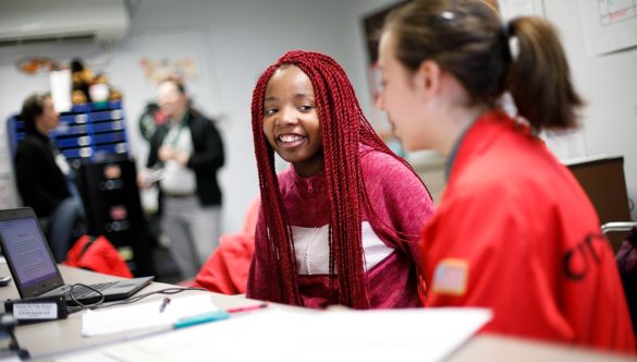 student is smiling at AmeriCorps member while doing work at computer in the classroom