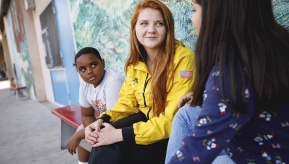 AmeriCorps member talking with a student on a bench while another student listens