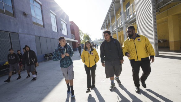 Two male middle school students walk alongside two City Year AmeriCorps members outside school on a sunny day