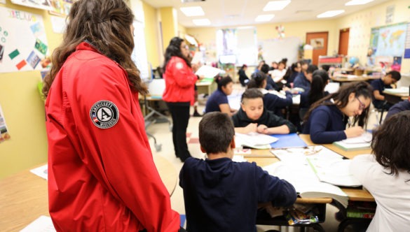 city year americorps members in a classroom helping students who are working with their desks pushed together