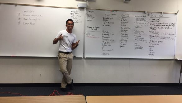 Paolo Aligada gives double thumbs-up while standing in front of a whiteboard covered in lesson plan strategies.
