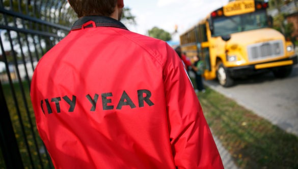 An AmeriCorps member watches students board school buses