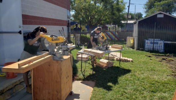 Two Care Force AmeriCorps Members cut wood using chop saws.